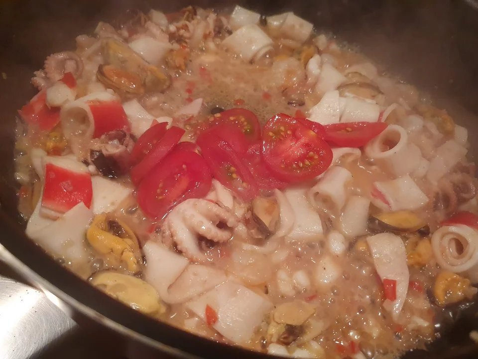 Roșii cherry tăiate adăugate peste cocktailul de fructe de mare